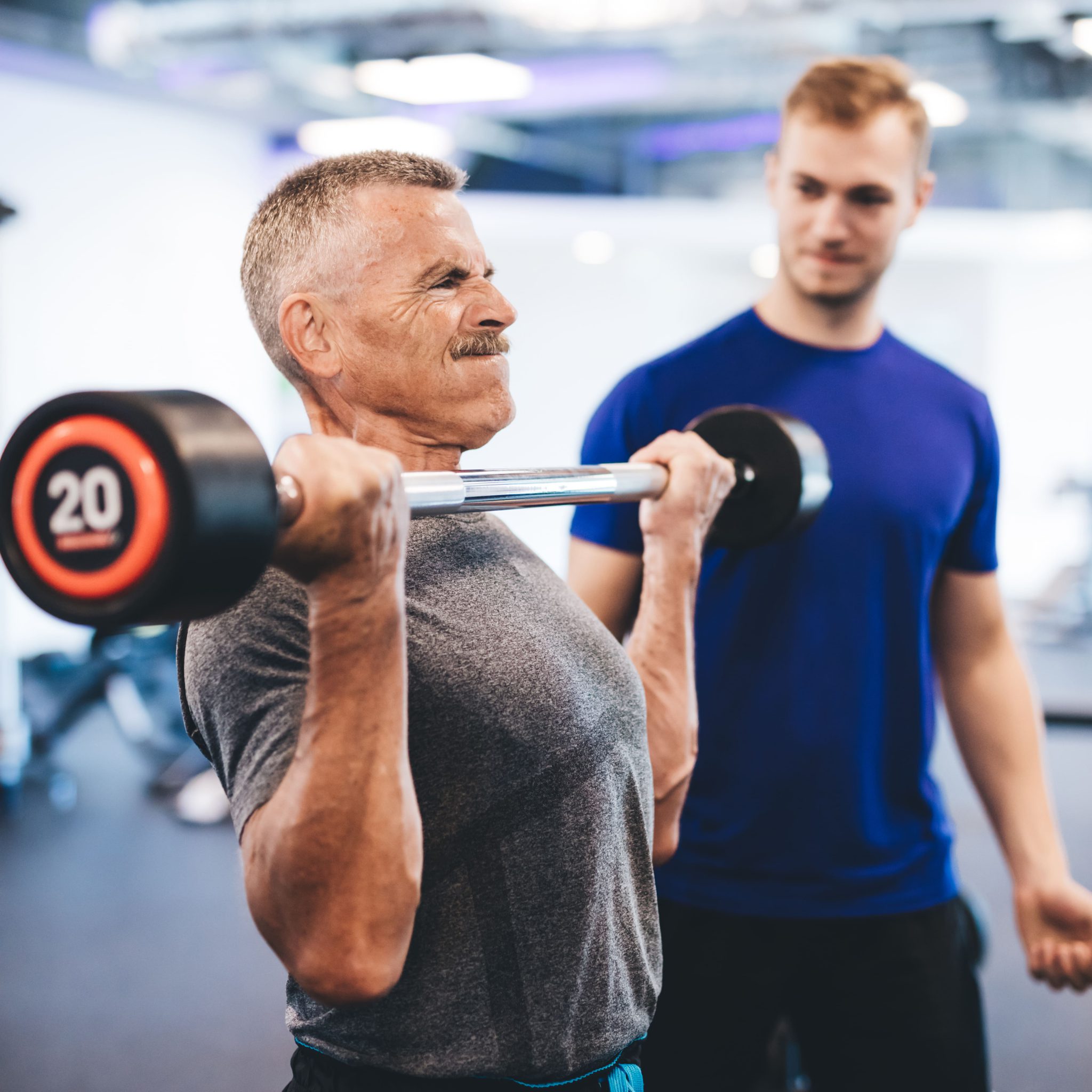 senior-man-weightlifting-assisted-by-personal-trai-YHDE5Z2